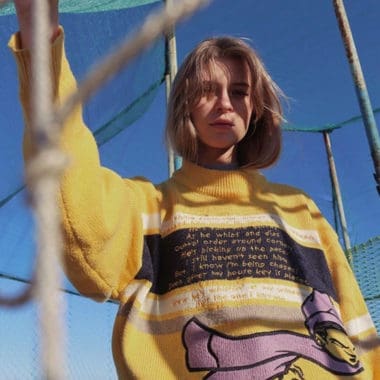 rosey blonde bob hair lady wearing oversized yellow knitted sweater standing in netted outdoor area rosey blonde bob hair lady wearing oversized yellow knitted sweater standing in netted outdoor area