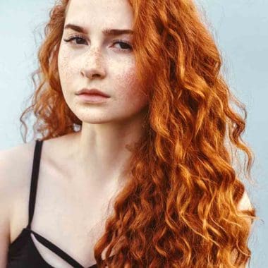 Flaming Copper_image 3 Long, curly, red head female with freckles, standing against white wall